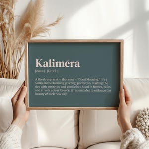 May include: A framed print with a teal background and white text. The text reads "Kaliméra [noun] [Greek] A Greek expression that means "Good Morning." It's a warm and welcoming greeting, perfect for starting the day with positivity and good vibes. Used in homes, cafes, and streets across Greece, it's a reminder to embrace the beauty of each new day."