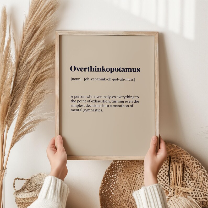May include: A beige framed print with the word "Overthinkopotamus" defined as "A person who overanalyses everything to the point of exhaustion, turning even the simplest decisions into a marathon of mental gymnastics."
