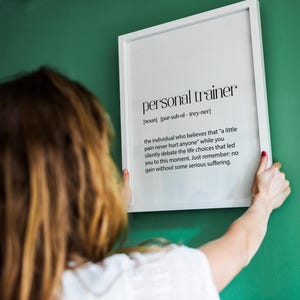 May include: A white framed print with the definition of "personal trainer" in black text. The definition reads: "the individual who believes that "a little pain never hurt anyone" while you silently debate the life choices that led you to this moment. Just remember: no gain without some serious suffering."