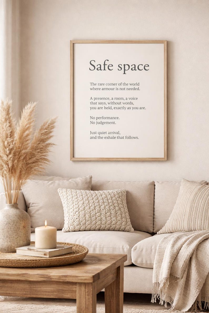 May include: A framed print with the words "Safe space" in a minimalist font. The print is displayed above a beige sofa with decorative pillows and a wooden coffee table. A vase with dried pampas grass and a lit candle add to the cozy atmosphere.