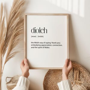 以下が含まれることがあります： 白い背景に黒い文字で「diolch」と書かれた額装されたプリント。この言葉は、感謝、つながり、ウェールズの精神を体現した「ありがとう」をウェールズ語で言う方法として定義されています。