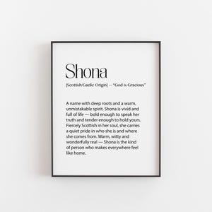 May include: A framed print featuring the name "Shona" in a decorative font. The text below explains the name's Scottish/Gaelic origin and meaning, and describes the name's characteristics. The frame is black.