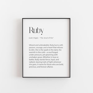 May include: A framed print with the name "Ruby" in a stylish font. The text below describes the name's meaning and origin, including phrases like "The Jewel of Fire" and "unshaken grace." The print is in a black frame.