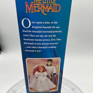 Pode incluir: Uma caixa para um conjunto de bonecas Disney's The Little Mermaid. A caixa apresenta um fundo azul com o t&iacute;tulo "Disney's The Little Mermaid" em texto branco. A caixa tamb&eacute;m apresenta uma imagem de Ariel e Eric em seus trajes de casamento. O texto na caixa diz: "Era uma vez, no reino debaixo do mar, vivia a bela princesa sereia, Ariel. Um dia ela conheceu o belo pr&iacute;ncipe humano, Eric. Eles se apaixonaram profundamente e se casaram... e que bela cerim&ocirc;nia de casamento foi!"