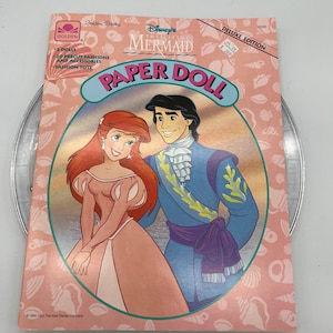 Puede incluir: Un libro de mu&ntilde;ecas de papel con La Sirenita de Disney. La portada presenta a Ariel y al Pr&iacute;ncipe Eric con sus atuendos formales. El libro incluye 2 mu&ntilde;ecas, 20 modas y accesorios precortados, y una bolsa de moda.