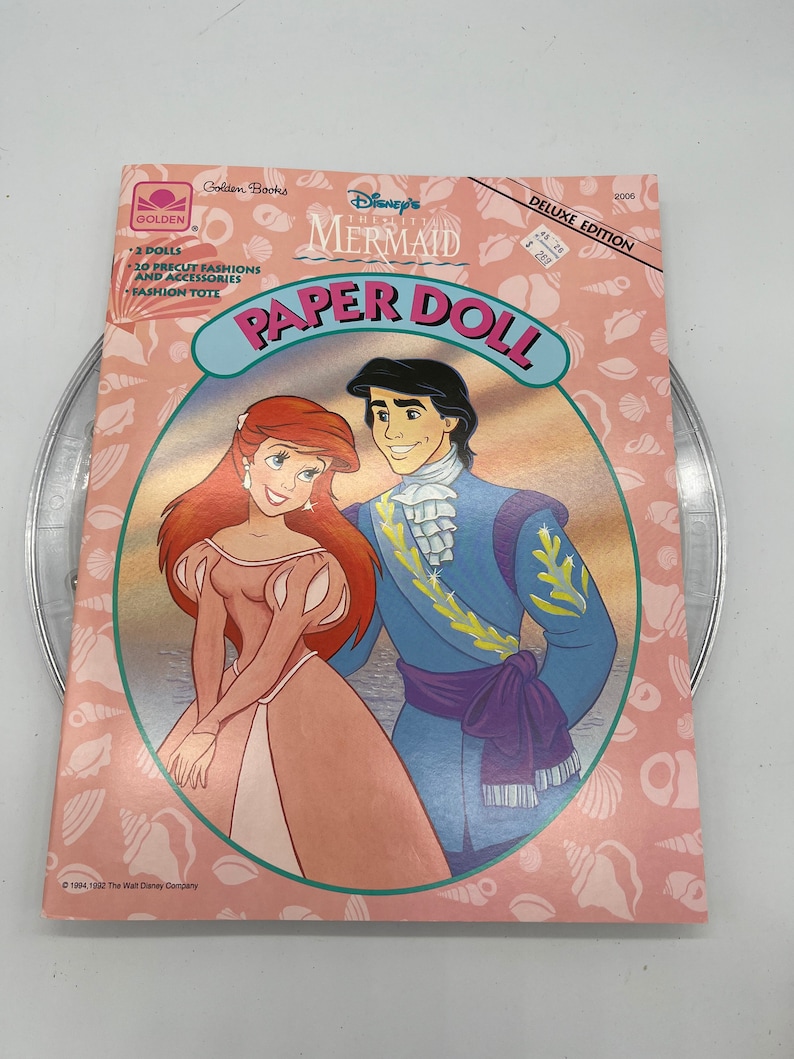 Puede incluir: Un libro de mu&ntilde;ecas de papel con La Sirenita de Disney. La portada presenta a Ariel y al Pr&iacute;ncipe Eric con sus atuendos formales. El libro incluye 2 mu&ntilde;ecas, 20 modas y accesorios precortados, y una bolsa de moda.