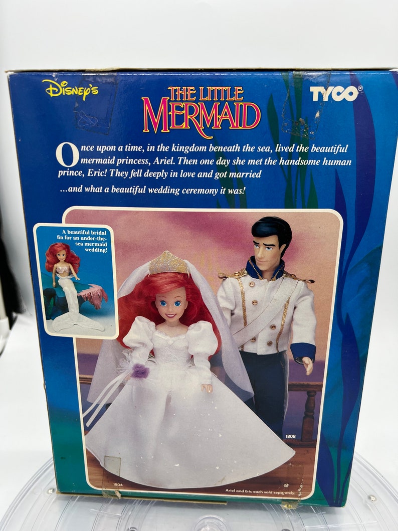 May include: A box for a Disney's The Little Mermaid wedding doll set. The box features Ariel and Eric in their wedding attire. The text on the box reads "Disney's The Little Mermaid" and "Once upon a time, in the kingdom beneath the sea, lived the beautiful mermaid princess, Ariel. Then one day she met the handsome human prince, Eric! They fell deeply in love and got married...and what a beautiful wedding ceremony it was!"