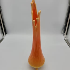 May include: A tall, orange glass vase with a unique, dripping design. The vase has a wide base and a narrow neck, and it is decorated with a textured, rippled pattern.