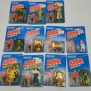 May include: A collection of ten vintage plastic dollhouse miniature figures from the world of Annie. The figures are packaged on individual cards with a blue background and the text "Knickerbocker The world of Annie Miniatures".