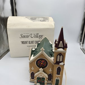 K&ouml;nnte beinhalten: Ein handbemaltes Keramik-Kirchengeb&auml;ude mit einem gr&uuml;nen Dach, Buntglasfenstern und einem hohen Turm. Die Kirche ist Teil der "Snow Village"-Kollektion und tr&auml;gt die Bezeichnung "Mount Olivet Church".