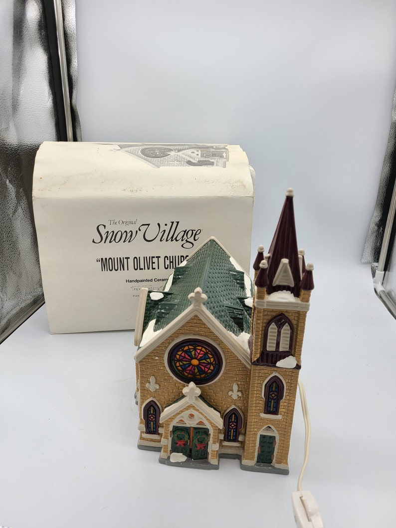 K&ouml;nnte beinhalten: Ein handbemaltes Keramik-Kirchengeb&auml;ude mit einem gr&uuml;nen Dach, Buntglasfenstern und einem hohen Turm. Die Kirche ist Teil der "Snow Village"-Kollektion und tr&auml;gt die Bezeichnung "Mount Olivet Church".