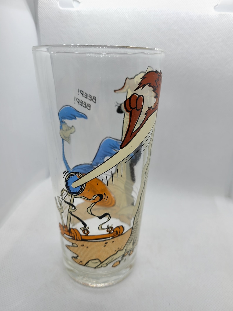 May include: A clear glass featuring a cartoon image of Wile E. Coyote chasing the Road Runner. The Road Runner is on a makeshift vehicle and the text "Beep! Beep!" is visible on the glass.