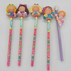 Peut inclure: Ensemble de cinq crayons vintage Cabbage Patch Kids avec des gommes colorées. Les crayons représentent différents personnages de Cabbage Patch Kids et ont des barils roses et violets avec un motif répétitif des personnages.