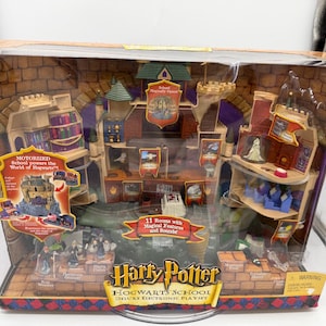 May include: A Harry Potter Hogwarts School Deluxe Electronic Playset in its original packaging. The box features a detailed castle structure with multiple rooms, small character figurines, and text including Motorized School powers the World of Hogwarts and 11 Rooms with Magical Features and Sounds.
