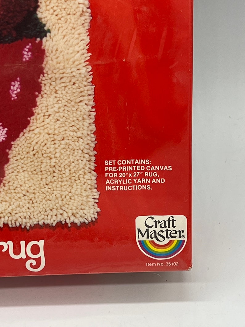 Puede incluir: Una caja roja con una alfombra blanca en su interior. La caja tiene el texto "Craft Master" y "Item No. 35102". El texto en la caja dice "Set contains: Pre-printed canvas for 20" x 27" rug, acrylic yarn and instructions."