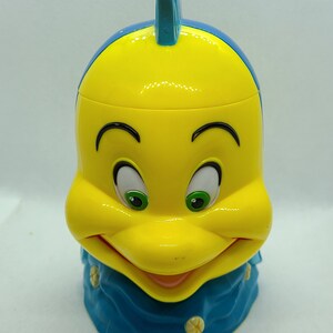 Puede incluir: Figurita de pl&aacute;stico amarilla y azul de un pez de dibujos animados con una cara sonriente. El pez tiene una aleta azul en la parte superior de la cabeza y una cola azul.