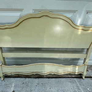 May include: A vintage white headboard with gold trim. The headboard has a curved top and a simple design.