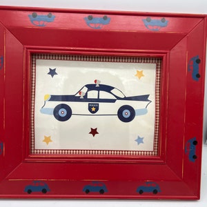 May include: A red wooden picture frame with a police car illustration. The frame has blue car accents and a gingham border. The police car is white and blue with a police badge and stars.