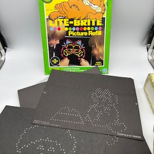 May include: A Garfield Lite-Brite picture refill box with 12 black and white picture sheets. The box features a cartoon image of Garfield the cat. The box says "America's No. 1 Cat" and "Lite-Brite Picture Refill".