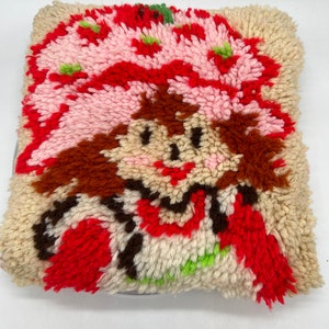 Op de afbeelding: Een vintage-stijl pluche kussen met een cartoon afbeelding van Strawberry Shortcake. Het kussen is gemaakt van een pluche, textuurrijke stof en heeft een rood, roze, wit, bruin en groen kleurenschema.