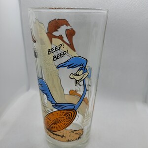 May include: A clear glass featuring a cartoon image of the Road Runner and Wile E. Coyote. The Road Runner is blue and running with a large orange disc. The text "Beep! Beep!" is printed on the glass.