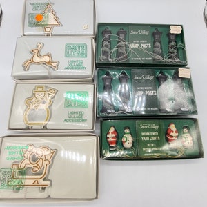 May include: Assortment of vintage Christmas decorations, including light-up village accessories and yard lights. The collection features a Christmas tree, reindeer, snowman, Santa Claus on a sleigh, and lamp posts. Each item is packaged in its original box.
