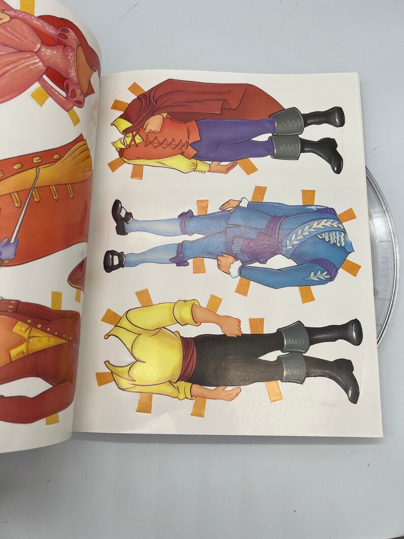 Puede incluir: Un libro de mu&ntilde;ecas de papel con cuatro mu&ntilde;ecas de papel diferentes. Las mu&ntilde;ecas est&aacute;n vestidas con diferentes atuendos, incluyendo un atuendo rojo y amarillo, un atuendo azul y amarillo y un atuendo amarillo y marr&oacute;n. Las mu&ntilde;ecas est&aacute;n todas de pie sobre un fondo blanco.