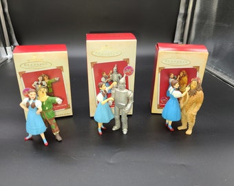 Peut inclure: Trois boîtes en carton rouge et blanc contenant chacune une décoration de Noël. Les décorations sont tirées du film Le Magicien d'Oz. La première décoration représente Dorothy et l'Épouvantail. La deuxième décoration représente Dorothy et l'Homme de Fer-Blanc. La troisième décoration représente Dorothy et le Lion peureux.