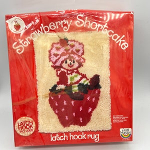 Puede incluir: Un kit de alfombra de gancho de cierre rojo y blanco con Strawberry Shortcake en una cesta de fresas. El kit incluye lienzo preimpreso, hilo acr&iacute;lico e instrucciones. Marca Craft Master.