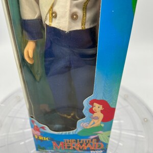 Pode incluir: Uma boneca vintage da Pequena Sereia em um uniforme azul e branco com detalhes dourados. A boneca est&aacute; embalada em uma caixa azul com uma imagem de Ariel na frente. A caixa diz "A Pequena Sereia" e "Tyco".
