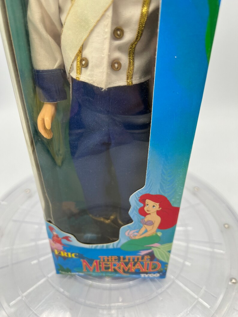 Pode incluir: Uma boneca vintage da Pequena Sereia em um uniforme azul e branco com detalhes dourados. A boneca est&aacute; embalada em uma caixa azul com uma imagem de Ariel na frente. A caixa diz "A Pequena Sereia" e "Tyco".