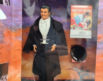 May include: A black and white doll of a man wearing a black suit and white shirt with a black bow tie. The doll is holding a black top hat. The doll is in a box with a poster for the movie Gone With The Wind.