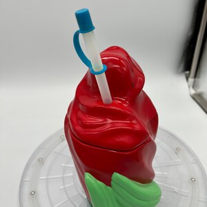 Op de afbeelding: Rode en groene plastic beker met een swirl-ontwerp. De beker heeft een doorzichtige rietje met een blauwe punt en een blauwe band.