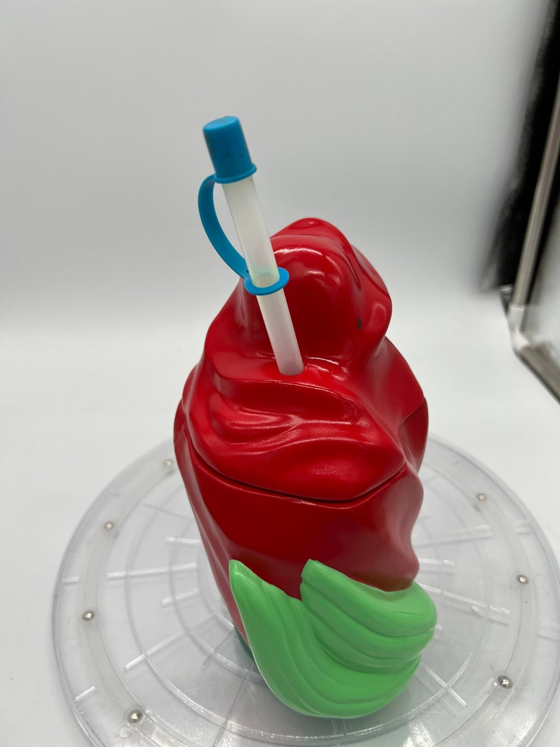 Op de afbeelding: Rode en groene plastic beker met een swirl-ontwerp. De beker heeft een doorzichtige rietje met een blauwe punt en een blauwe band.