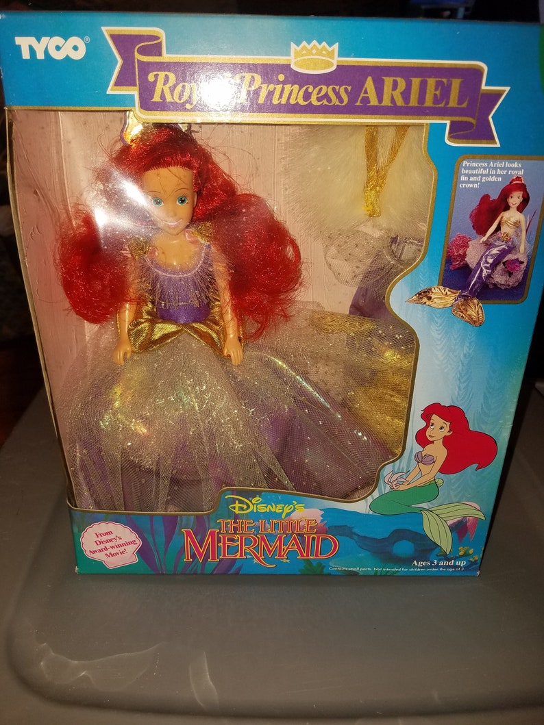 May include: A plastic doll of Ariel from Disney's The Little Mermaid, dressed in a purple and gold gown with a crown. The doll is packaged in a box with a picture of Ariel on the front. The box also includes the text "Disney's The Little Mermaid" and "Ages 3 and up".