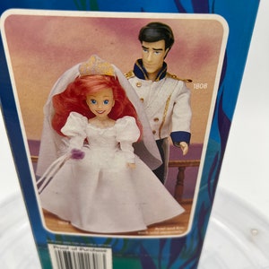 Pode incluir: Um conjunto de bonecas com tema de casamento com Ariel e o Pr&iacute;ncipe Eric da A Pequena Sereia da Disney. As bonecas est&atilde;o vestidas com trajes de casamento brancos e seguram um buqu&ecirc; de flores. A caixa tem o n&uacute;mero 1808 impresso.