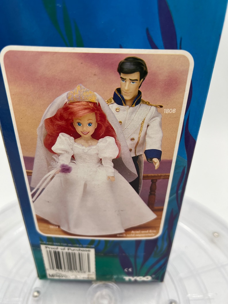 Pode incluir: Um conjunto de bonecas com tema de casamento com Ariel e o Pr&iacute;ncipe Eric da A Pequena Sereia da Disney. As bonecas est&atilde;o vestidas com trajes de casamento brancos e seguram um buqu&ecirc; de flores. A caixa tem o n&uacute;mero 1808 impresso.