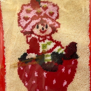 Puede incluir: Un kit de manualidades de fieltro rojo y blanco con una ni&ntilde;a de dibujos animados con una corona de flores rosas sentada en una fresa. El kit incluye todos los materiales necesarios para completar la manualidad.