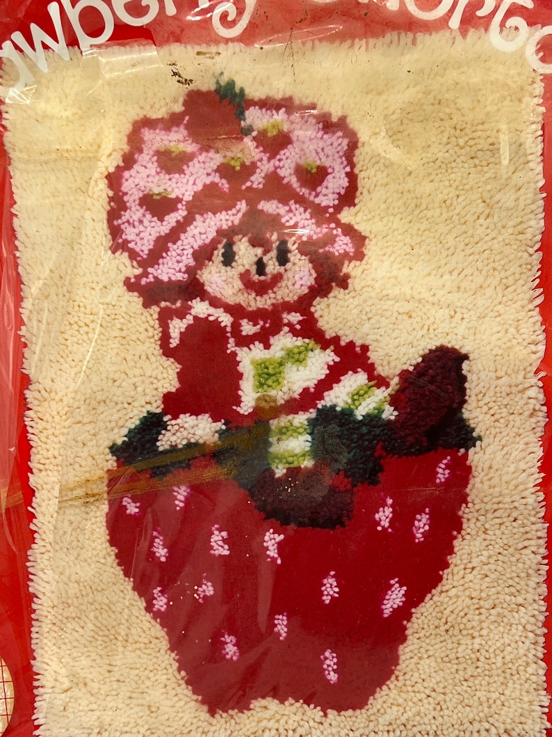 Puede incluir: Un kit de manualidades de fieltro rojo y blanco con una ni&ntilde;a de dibujos animados con una corona de flores rosas sentada en una fresa. El kit incluye todos los materiales necesarios para completar la manualidad.