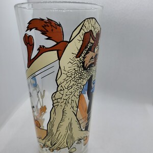 May include: A clear glass featuring a cartoon image of Wile E. Coyote and the Road Runner. The Road Runner is running away from Wile E. Coyote, who is holding a large rock. The glass is a vintage collectible.