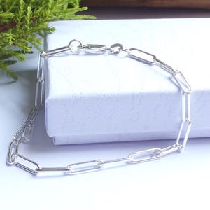 May include: A silver-toned chain bracelet featuring elongated, rectangular paperclip-style links. The bracelet is constructed with a series of uniform, polished metal links connected in a continuous loop, finished with a small circular clasp.