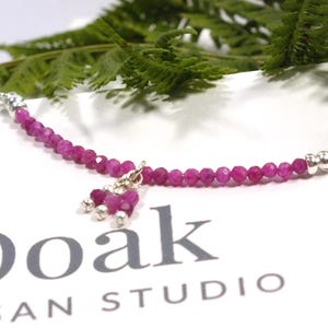 Puede incluir: Una pulsera con pequeñas cuentas de piedras preciosas facetadas de color rosa vibrante ensartadas en un alambre, acentuadas con cuentas de metal plateado y un dije central colgante hecho de cuentas rosas a juego y pequeñas esferas plateadas.