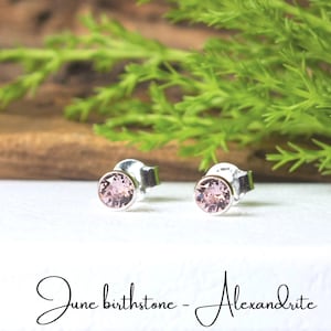 May include: A pair of silver stud earrings featuring round, faceted, light pink alexandrite stones in a bezel setting. The text below the earrings reads: June birthstone - Alexandrite. These earrings have a simple, circular design.