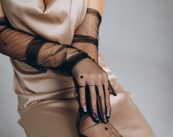 May include: A woman wearing a beige satin dress with a black beaded necklace and black mesh gloves with black beads.
