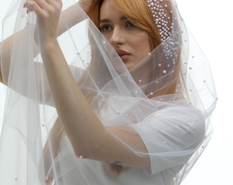 May include: A white tulle veil with pearl embellishments. The veil is draped over a person's head and shoulders.