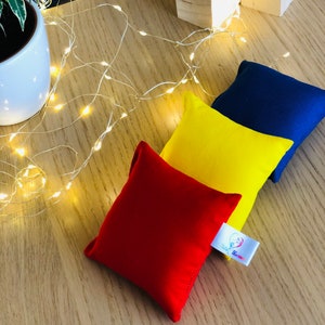 Puede incluir: Tres bolsas de frijoles de tela en rojo, amarillo y azul. Las bolsas de frijoles est&aacute;n sobre una superficie de madera con una cadena de luces blancas. Las bolsas de frijoles tienen una etiqueta blanca con un coraz&oacute;n rojo y el texto "Play Time!"