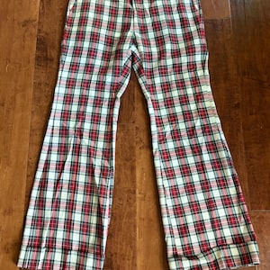 May include: A pair of plaid pants in a red, white, and black pattern. The pants have a flared leg design and a classic plaid pattern. The pants are made of a lightweight fabric, suitable for casual wear.