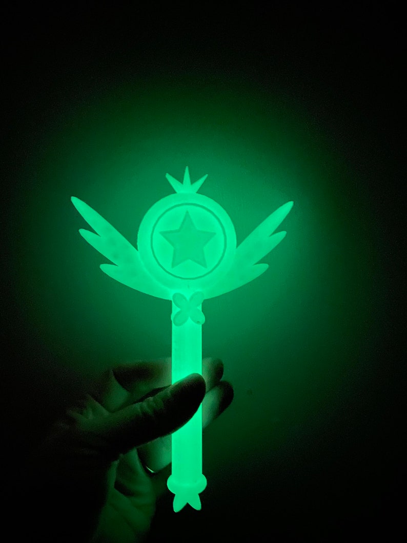 May include: A green glow-in-the-dark wand with a star and wings. The wand is made of plastic and has a smooth surface.