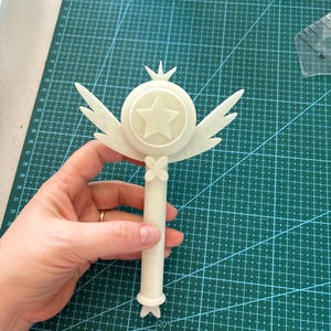 May include: A white plastic wand with a star-shaped top and wings. The wand is about 12 inches long.