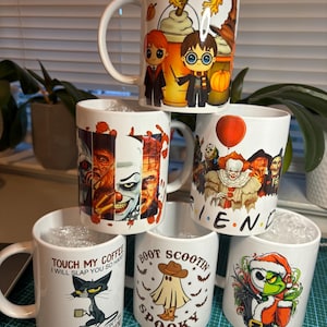 Pode incluir: Um conjunto de seis canecas de cerâmica branca com vários desenhos temáticos de Halloween. As canecas apresentam personagens de Harry Potter, It, O Estranho Mundo de Jack e outros filmes de terror populares. As canecas estão empilhadas em forma de pirâmide.